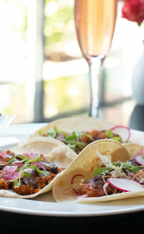 three tacos plated next to tall glass of champagne