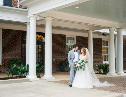 bride and groom smiling outside of exterior of The Mayton hotel