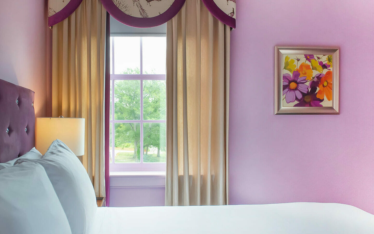 pink hotel bedroom with flower artwork hung on the wall next to window