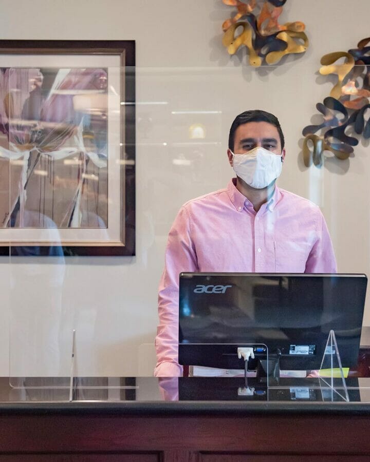 protected front desk area of receptionist behind computer wearing mask