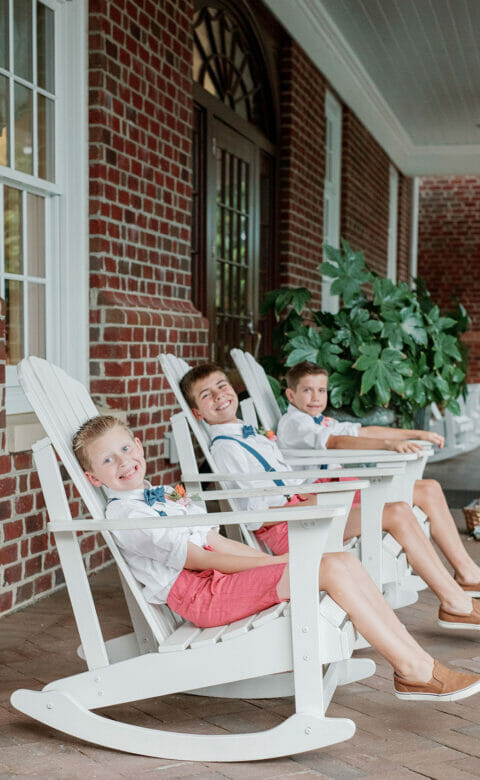 three young boys dressed for a wedding, smiling and sitting on rocking chairs on a terrace